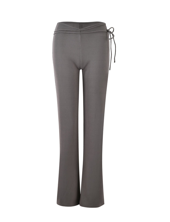 The image showcases a pair of REY PANT - GREY : CHARCOAL by TIGERMIST, featuring a slight flare at the bottom. These pants boast a fitted waistband, accented with a drawstring on the right side. The fabric seems soft and slightly stretchy, ensuring a comfortable and relaxed fit.
