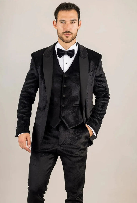 Man wearing a black velvet tuxedo suit with satin lapels, white dress shirt, black bow tie, and black dress shoes, standing against a plain background.