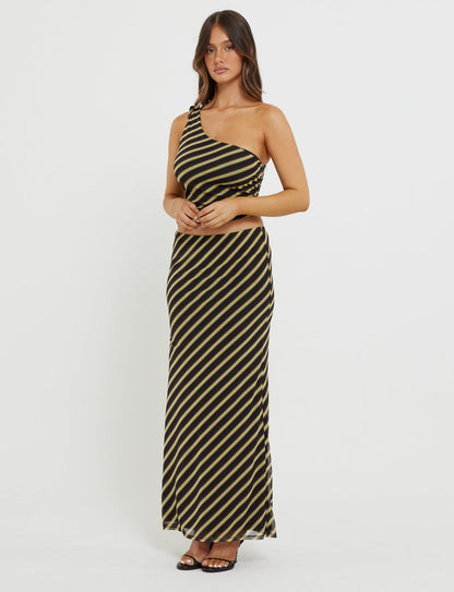 A person with long brown hair is wearing the Deanna Maxi Skirt in Brown Stripe from TIGERMIST. They are standing against a plain white background with their hands clasped below their chest, and are adorned in black open-toed heels.