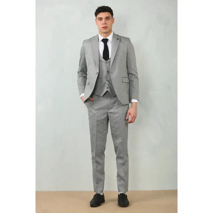Male model in grey tailored fit wedding 3-piece suit with a matching blazer, vest, and trousers, paired with a white shirt and black shoes, standing against a plain background.
