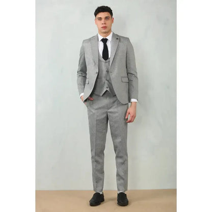 Male model in grey tailored fit wedding 3-piece suit with a matching blazer, vest, and trousers, paired with a white shirt and black shoes, standing against a plain background.