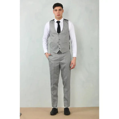 Back view of a man in a grey tailored fit wedding 3-piece suit with a white shirt, black shoes, and a black vest, standing against a plain wall.