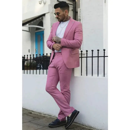 Man wearing a pink tailored fit suit with a white shirt, dark tie, sunglasses, and tattoos, showcasing a modern fashion statement.