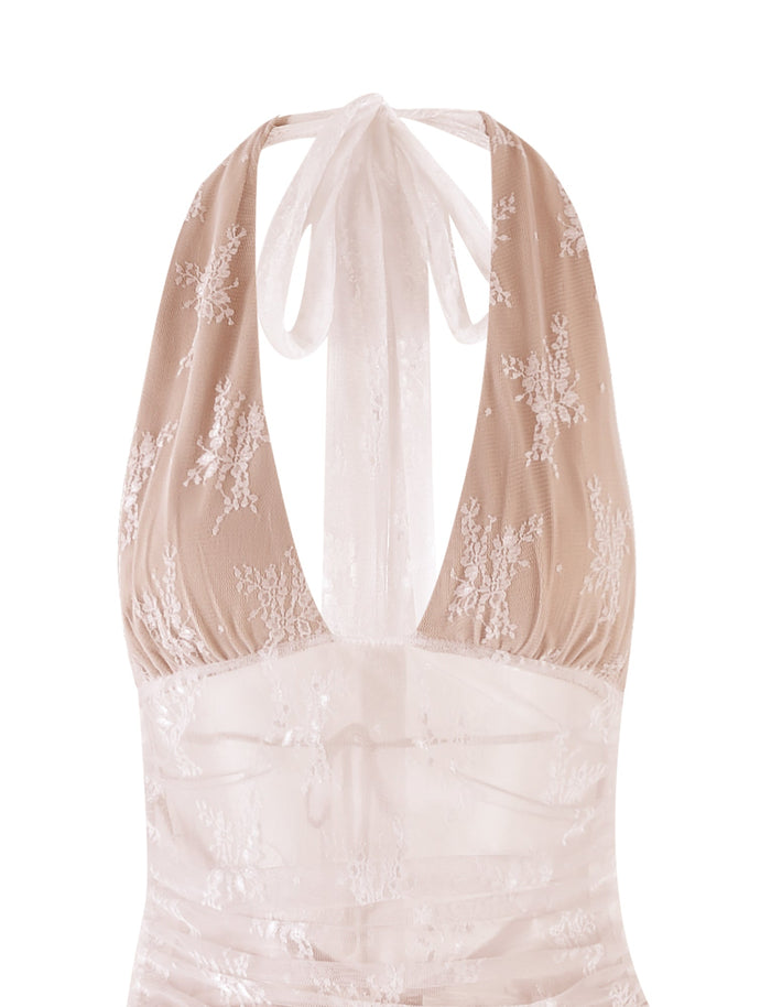 A close-up of the LENORA LACE DRESS - WHITE from TIGERMIST showcases its halter neckline and intricate floral lace patterns on a sheer fabric. The back ties into a bow at the neck, adding a delicate and elegant touch to the overall design.