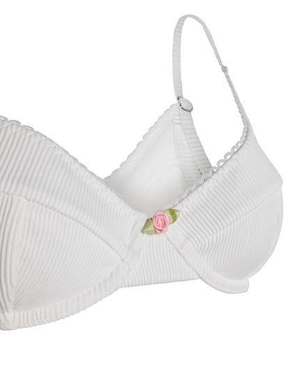 The MILANA BIKINI TOP - WHITE by TIGERMIST is a white ribbed swim top with adjustable straps, a pink rose at the center front, and a soft, seamless design for comfort without visible fasteners.