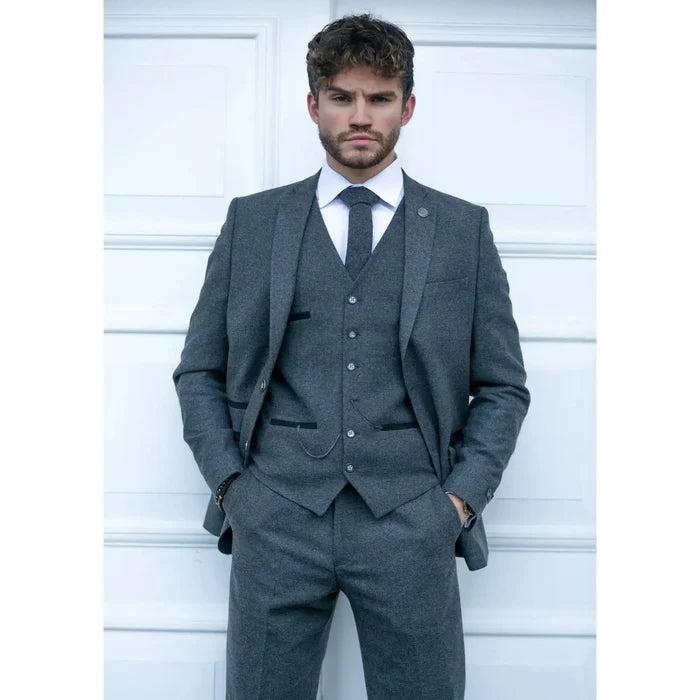 Man wearing a dark grey tailored wool tweed suit with matching trousers, white shirt, and red tie, classic formal look for business or events.