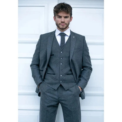 Man wearing a dark grey tailored wool tweed suit with matching trousers, white shirt, and red tie, classic formal look for business or events.