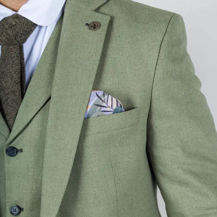 Male model in sage green linen suit with white shirt and dark tie, standing outdoors with hands in pockets for a stylish look