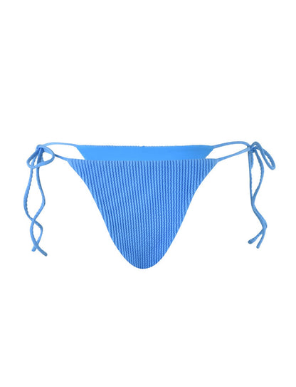 The YVE BIKINI BOTTOM - BLUE from TIGERMIST, in a royal blue hue, features ribbed fabric and adjustable side tie strings. The bikini bottom is displayed against a white background, showcasing its textured material and the customizable fit provided by the ties on both sides.